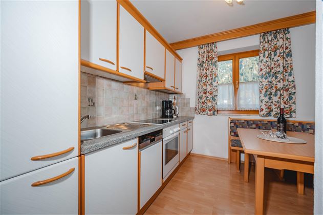 A modern kitchen with bright cabinets and an edible dining area. The windows are decorated with floral curtains.