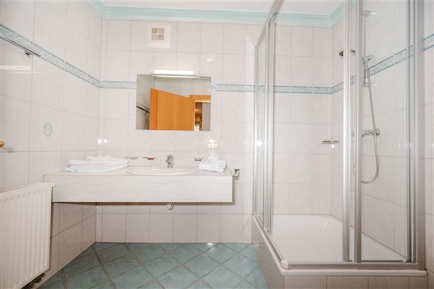 A modern bathroom with white tiles and a shower. Fresh towels are ready on the sink.