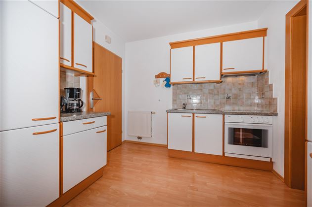 A modern kitchen with white furniture and wooden accents. It is bright and well equipped with appliances such as a stove and a coffee maker.