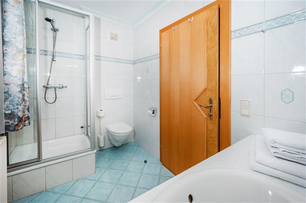 A modern bathroom with a shower, a toilet, and a bathtub. The walls are brightly tiled and there are fresh towels.