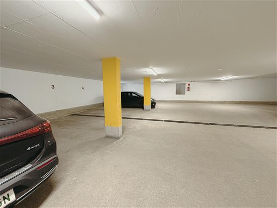 A parking garage with multiple parking spaces. Two cars are standing in a bright, spacious room.