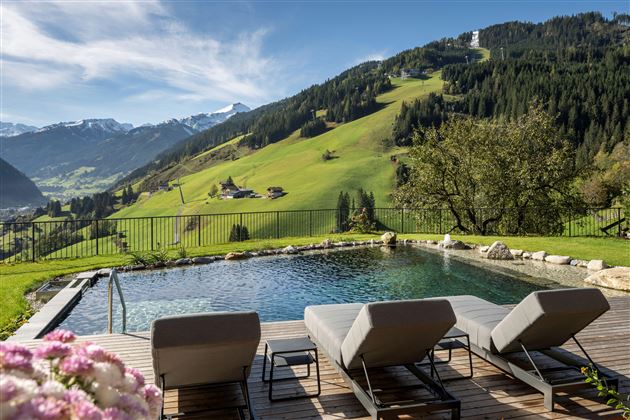 Ein ruhiger Außenbereich mit einem Schwimmbecken, Liegen und einer schönen Aussicht auf grüne Hügel und Berge. Der Himmel ist klar und sonnig.