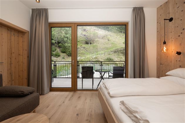 Ein modernes Zimmer mit einem großen Fenster und Blick auf die Natur. Die Einrichtung ist gemütlich mit einem Doppelbett und einer sitzenden Ecke.