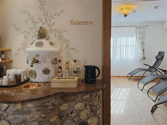 An inviting wellness area with a stone counter and a tea station. In the background, there are comfortable loungers and large windows that allow plenty of light.