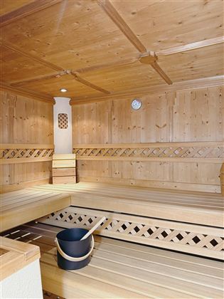 A cozy sauna with wooden interior and benches for relaxing. A bucket and a clock complete the atmosphere.