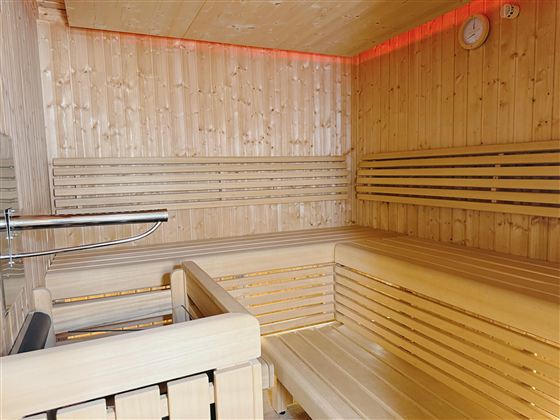 A modern sauna with wooden paneling and comfortable benches. Soft light radiates from the wall, creating a relaxing atmosphere.
