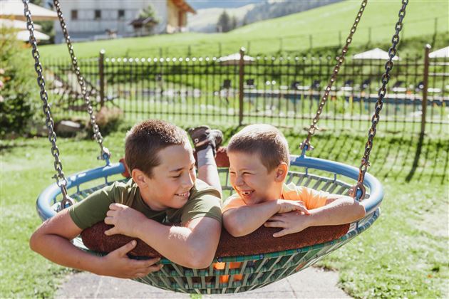 Two happy boys are lying together in a swing seat. They are laughing and enjoying their time outdoors.
