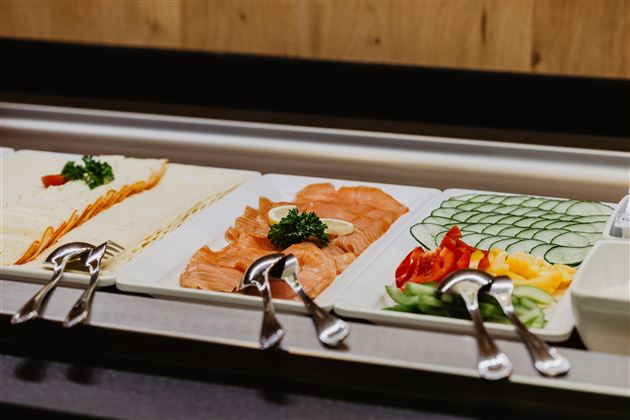 A beautifully arranged buffet with various food options. These include cold cuts, smoked salmon, fresh vegetables, and herbs.