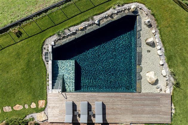 Ein moderner Pool in einem gepflegten Garten. Rasenflächen und Steine umgeben den Poolbereich.