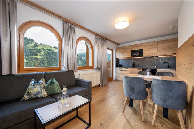 A modern apartment with a cozy seating area and a kitchen. Large windows offer a view of the green mountain landscape.