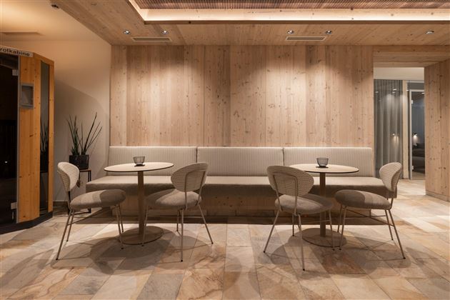 Ein modernes Café mit hellem Holzinterieur und stilvollen Sitzgelegenheiten. Zwei runde Tische sind platziert, umgeben von eleganten Stühlen.