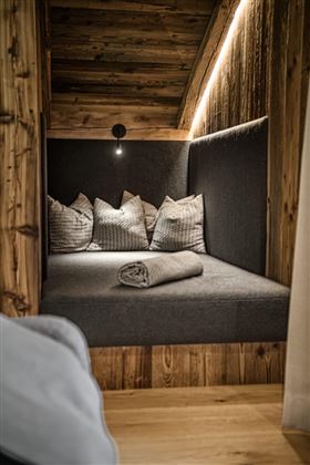 A cozy seating area with dark gray upholstery and several cushions. The wood and soft lighting create a warm atmosphere.