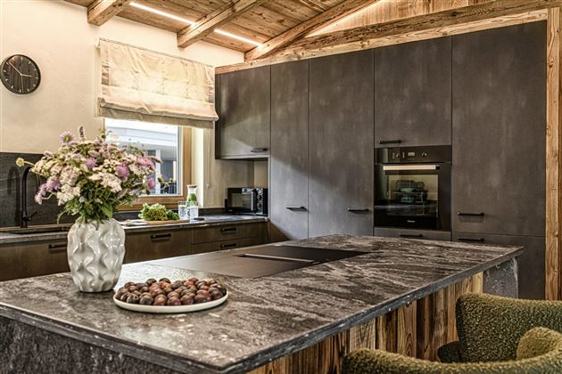 A modern kitchen with wood and concrete accents. On the countertop, there is a vase of flowers and a bowl of nuts.
