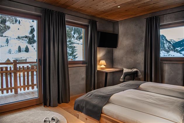 A cozy bedroom with two beds and a beautiful view of the snowy landscape. Large windows and modern furnishings create an inviting atmosphere.