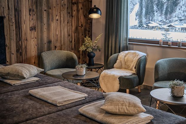 A cozy relaxation room with modern armchairs and a view of a snowy landscape. The warm wood tones and soft textiles create an inviting atmosphere.