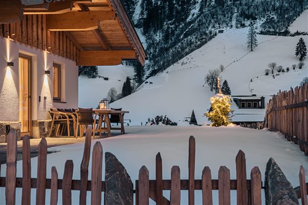 A cozy building in the wintry landscape. The garden is covered in snow, and a small Christmas light shines in the dark.
