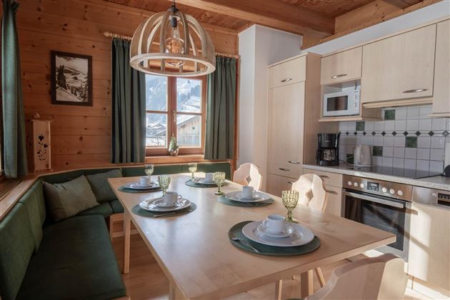 Eine gemütliche Küche mit Holzverkleidung und einem großen Tisch. Der Tisch ist für eine Mahlzeit gedeckt, mit Geschirr und Gläsern, und es gibt ein Fenster mit Blick auf die Natur.