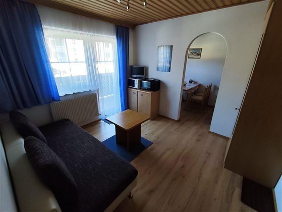 Ein gemütliches Wohnzimmer mit einem Sofa und einem Tisch. Rechts ist ein Durchgang zu einem Essbereich.