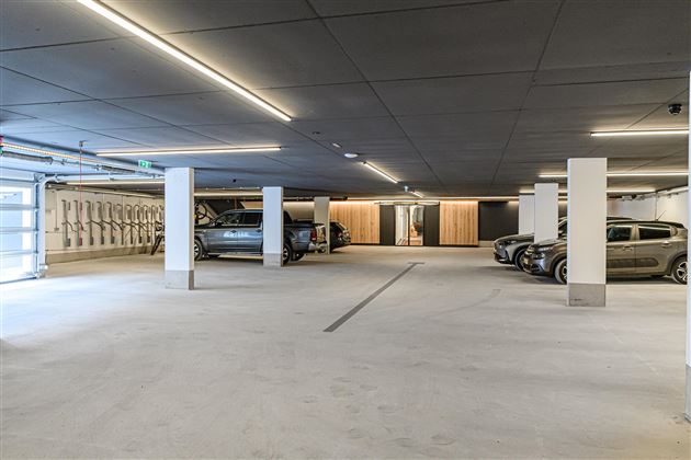 A modern underground parking garage with several parked cars. The lighting is bright and the design is minimalist.