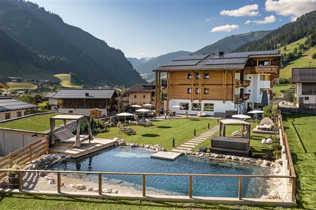 A modern holiday home with a large pool in the foreground. The surroundings are green and surrounded by mountains.