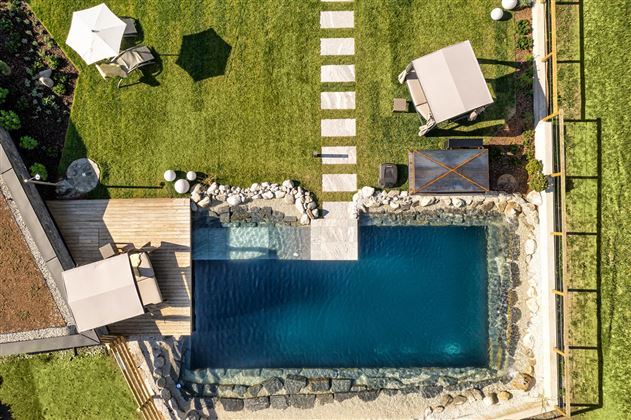 A beautiful pool in the garden, surrounded by lawn and paved paths. Relaxed atmosphere with loungers and sun umbrellas.