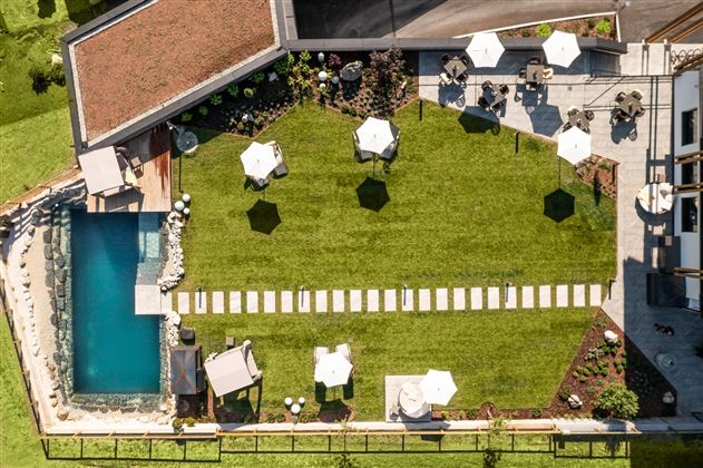 A well-maintained garden with a lawn area and several loungers. Next to the garden is a pool and sunny seating areas with umbrellas.