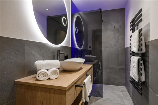 Ein modernes Badezimmer mit einer Holzkommode und einem großen Waschbecken. Die Wände sind in Grautönen gehalten und es gibt eine stilvolle Beleuchtung.