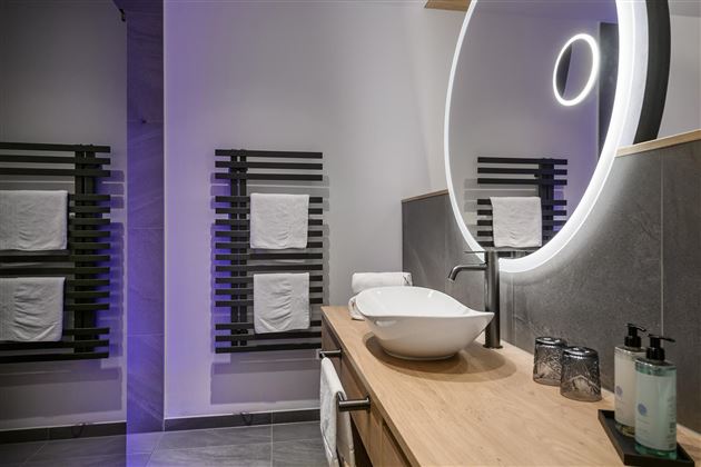 Ein modernes Badezimmer mit einer eleganten Waschschüssel und einem beleuchteten Spiegel. Handtücher sind an einem stilvollen Handtuchhalter aufgehängt.