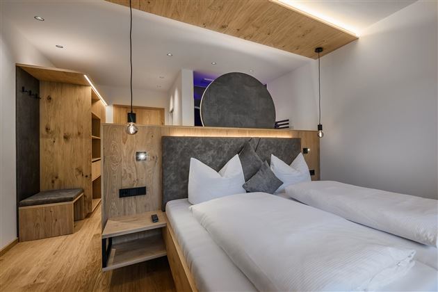 Ein modernes Schlafzimmer mit einem Doppelbett und Holzverkleidungen. Die gemütliche Atmosphäre wird durch sanfte Beleuchtung und stilvolle Dekorationen unterstrichen.
