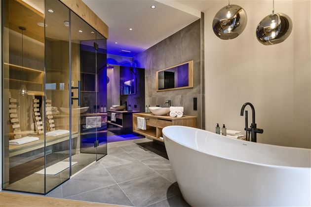 Ein modernes Badezimmer mit einer freistehenden Badewanne und einer Glasduschkabine. Die Wände sind in neutralen Tönen gehalten und es gibt stilvolle Beleuchtungselemente.
