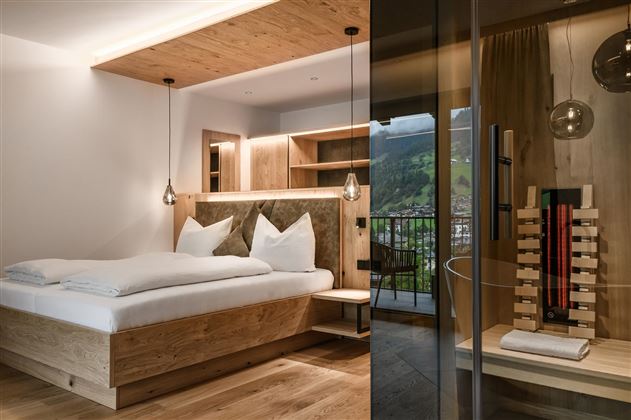 Ein modernes Schlafzimmer mit einem großen Bett aus Holz und klaren Linien. Stilvolle Beleuchtung und eine glasbekleidete Ecke sorgen für ein elegantes Ambiente.
