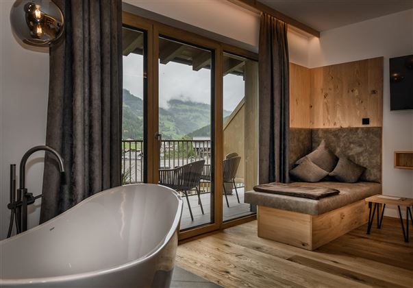 Ein modernes Zimmer mit einer freistehenden Badewanne und einem gemütlichen Sitzbereich. Große Fenster bieten einen Blick auf die Berge.