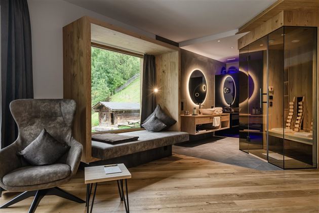 Ein modernes Zimmer mit großen Fenstern und einer gemütlichen Sitzecke. Die Sauna ist ebenfalls gut sichtbar und fügt dem Raum eine entspannende Atmosphäre hinzu.