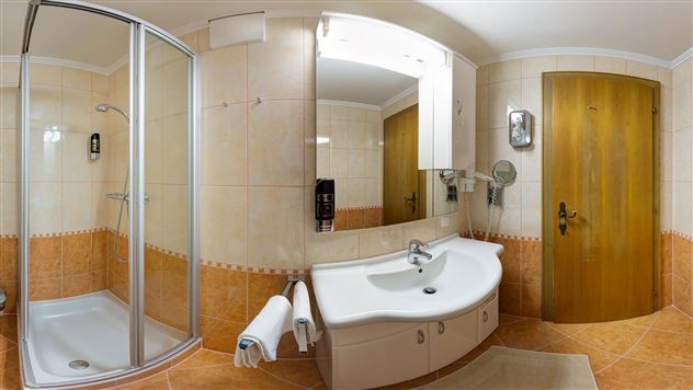 A modern bathroom with a shower and a sink. The walls are light tiled and there is a large mirror.