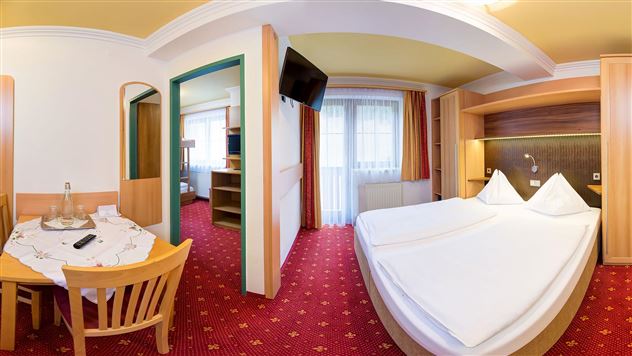 A cozy hotel room with a double bed and a table. The room has large windows and a warm color scheme.