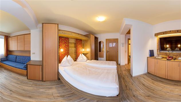 A cozy hotel room with two beds and an additional sofa bed. The decor is modern and bright with wooden details.