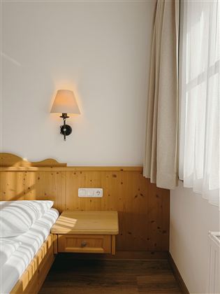 A cozy room with a wooden bed and a soft light source. The room is bright and friendly, with a window and a curtain.