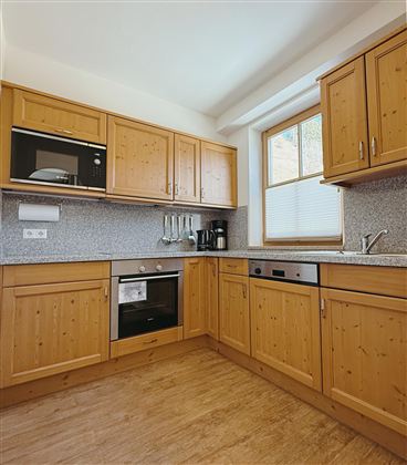 A modern kitchen with wooden cabinets and gray countertops. It is well equipped with an oven, a microwave, and a coffee machine.