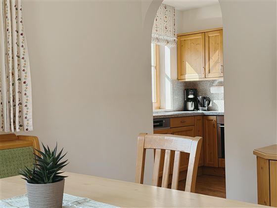 A cozy kitchen with wooden cabinets and bright light. On the table is a small pot with a plant.