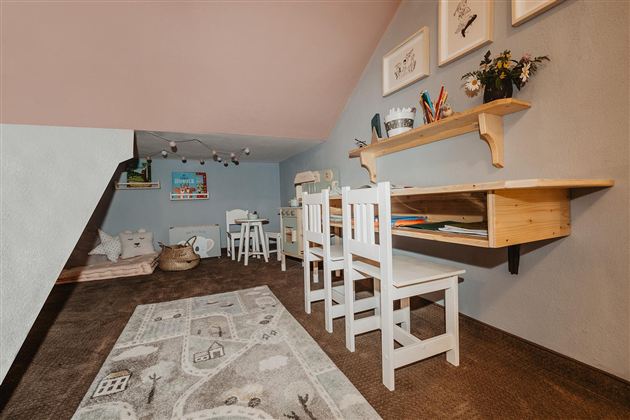 Ein gemütliches Dachzimmer mit einer hellen Arbeitsfläche und mehreren Stühlen. An der Wand hängen Bilder und Blumen in einer Vase.