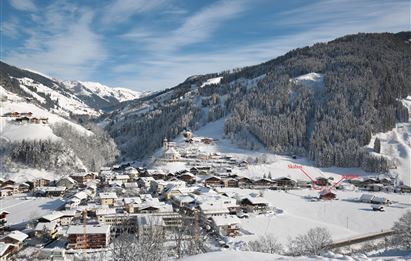 Ein malerisches Bergdorf im Winter, umgeben von schneebedeckten Hügeln und Bergen. Die darunter liegenden Häuser sind in eine sanfte weiße Decke gehüllt.