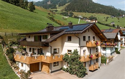 A beautiful house in the mountains with a large balcony and colorful flowers. The surroundings are green and hilly, ideal for a peaceful retreat.