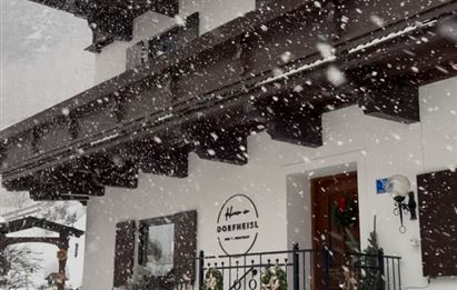 Ein traditionelles alpenländisches Haus mit einem Holzbalkon. Es schneit kräftig und der Boden ist mit Schnee bedeckt.