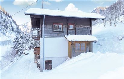 Ein charmantes Holzhaus im Schnee, umgeben von einer winterlichen Landschaft. Der Himmel ist klar und die Berge sind im Hintergrund sichtbar.