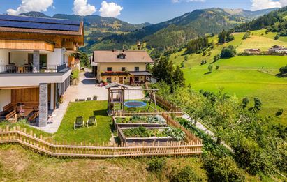 Ein malerisches Grundstück mit modernen Häusern und einem Garten. Die Umgebung ist grün und von Bergen umgeben, unter einem klaren Himmel.