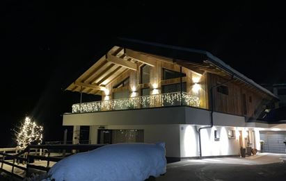 Ein modernes Holzhaus mit festlicher Beleuchtung. Der Schnee liegt friedlich auf dem Boden und der Himmel ist dunkel.