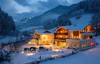 A cozy hotel in a snow-covered landscape. The lights of the hotel shine in the twilight, creating an inviting atmosphere.