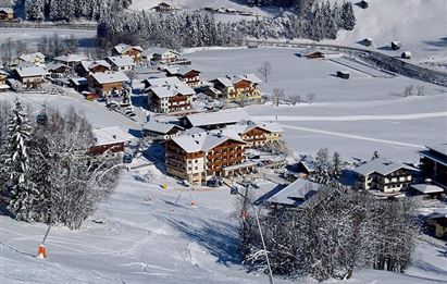 Eine malerische Berglandschaft mit einem schneebedeckten Dorf. Skilifte und Häuser sind umgeben von schneebedeckten Bäumen.