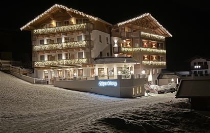 A cozy hotel, festively lit at night. It is surrounded by snow and radiates a warm atmosphere.