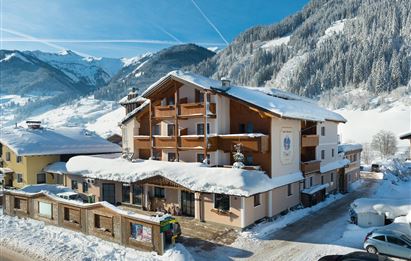 A cozy hotel in the snow with large windows and balconies. In the background, snow-covered mountains can be seen.